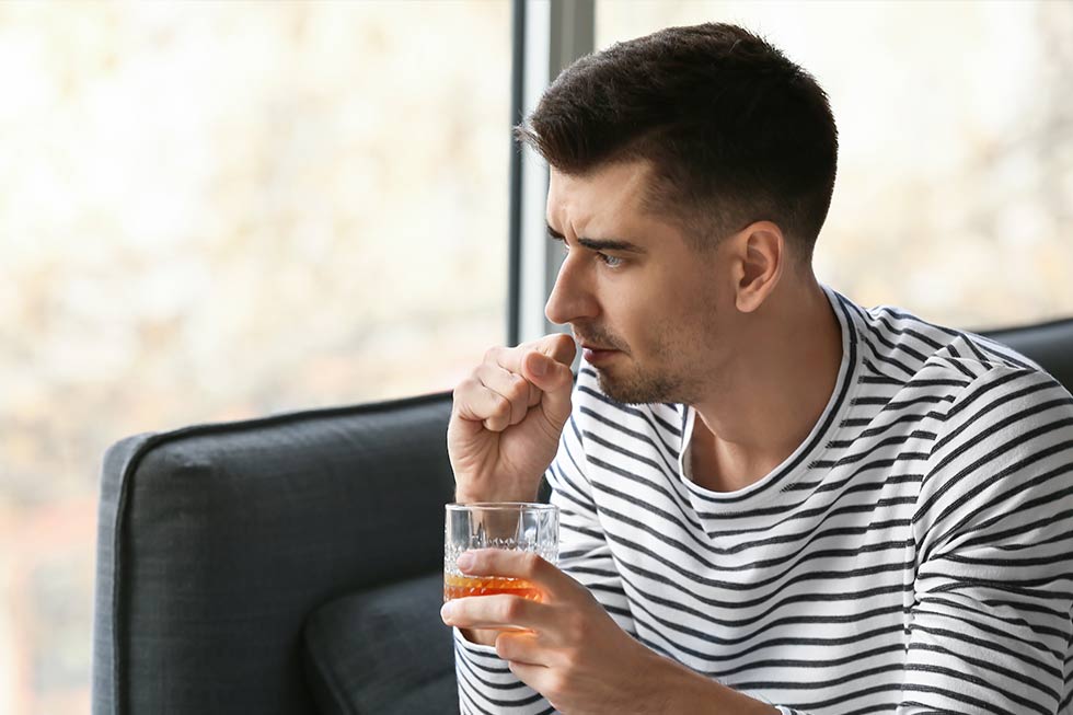 man conflicted about alcoholism having a drink inside by a window
