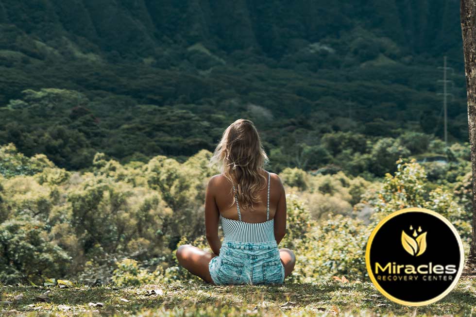 woman sitting in a wooded area in a meditation pose